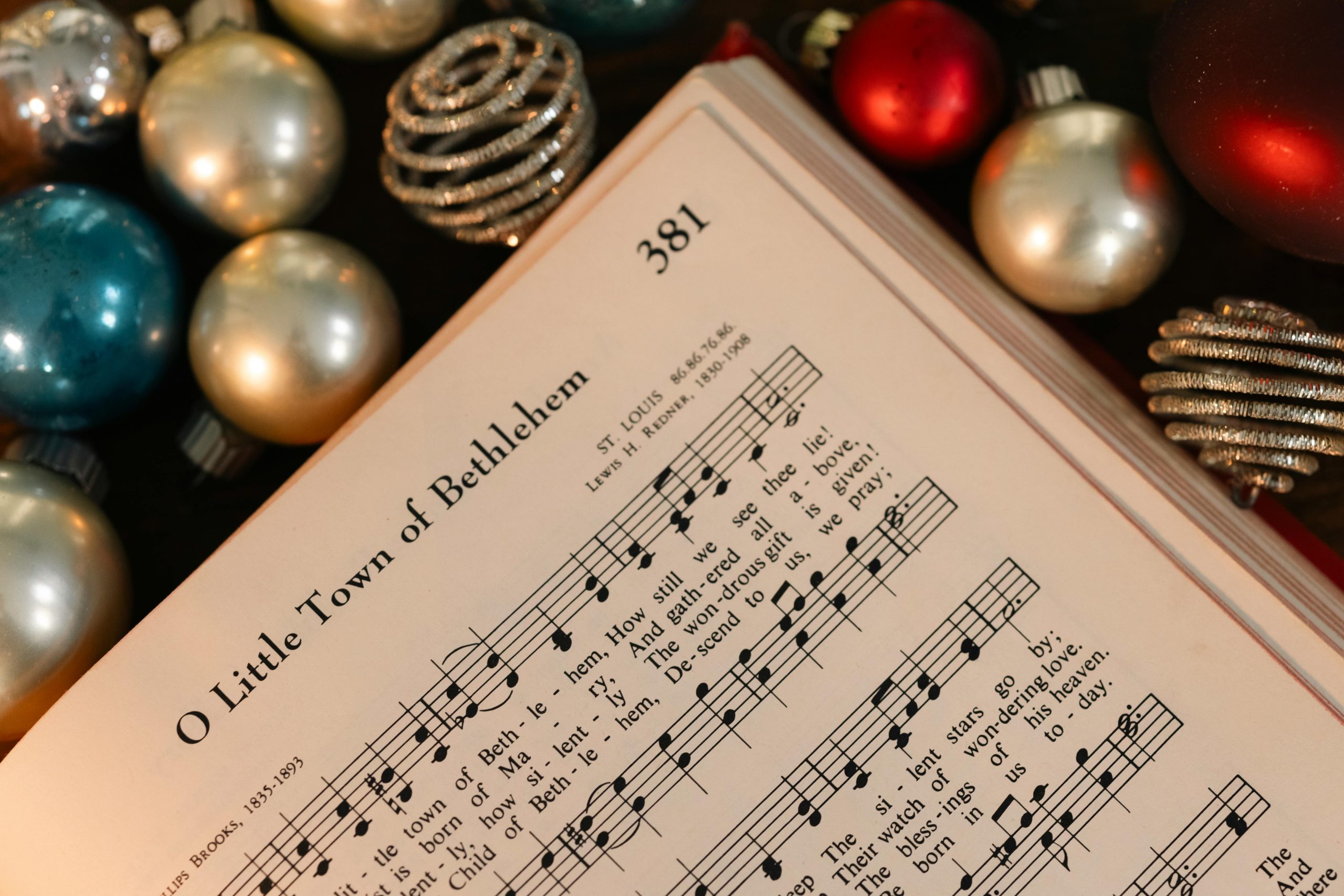 Open hymnbook displaying 'O Little Town of Bethlehem' surrounded by festive holiday baubles.