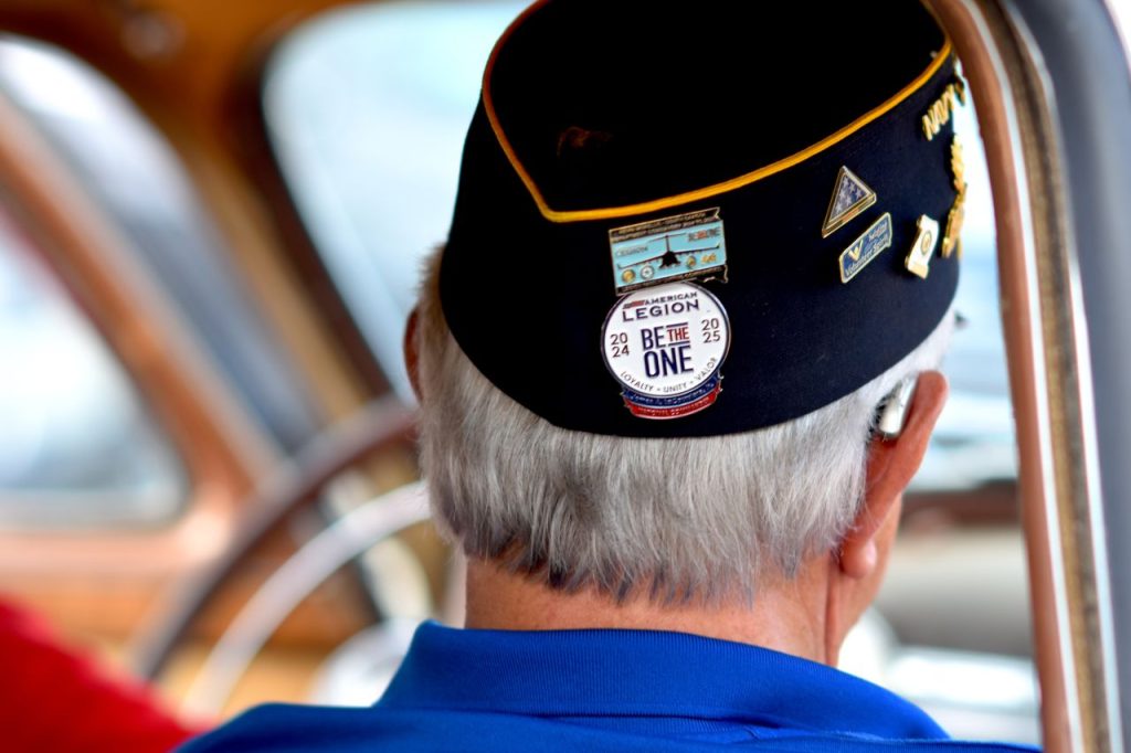 Close-up of a veteran wearing a decorated American Legion cap inside a vehicle.